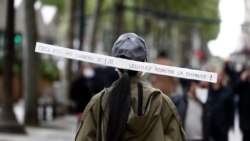 Žena nosi natpis 'Ovo je kapa od jednog metra. Molim vas da zadržite udaljenost', dok šeta avenijom Champs Elysee u Parizu, Francuska, 11. maja 2020. godine.