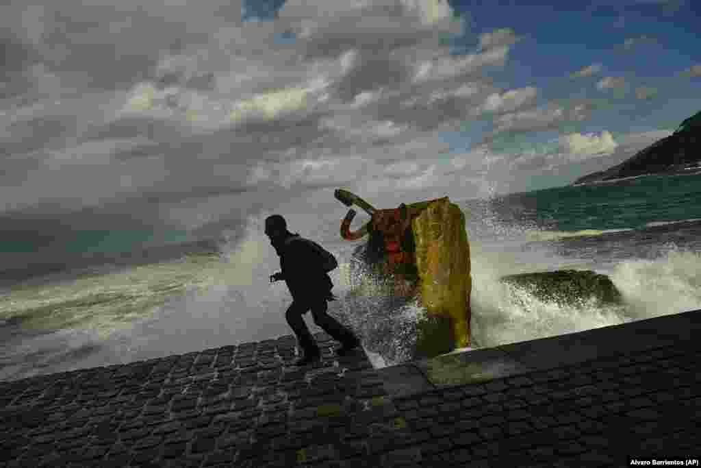 A man runs as a giant wave crashes against the sea defenses during high tide in San Sebastian, Spain. (AP/Alvaro Barrientos)