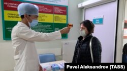 Медработник замеряет температуру тела посетителя больницы.