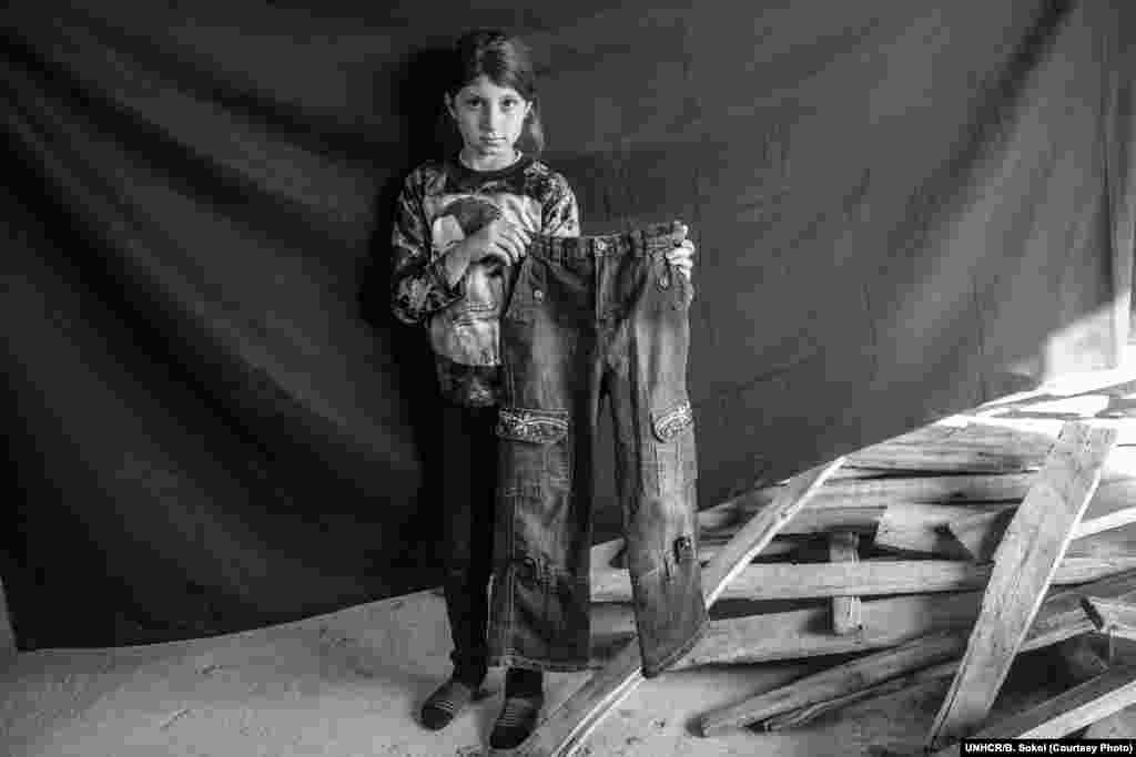 Leila*, 9, poses for a portrait in the urban structure where she and her family are taking shelter in Erbil, in the Kurdistan Region of Iraq, on 17 November 2012. Together with her four sisters, mother, father and grandmother, Leila arrived in Erbil five days before this photograph was taken, after fleeing their home in Deir Alzur, Syria. The most important thing Leila was able to bring with her are the jeans she holds in this photograph. "I went shopping with my parents one day and looked for hours without finding anything I liked. But when I saw these, I knew instantly that these were perfect because they have a flower on them, and I love flowers." She has only worn the jeans three times, all in Syria – twice to wedding parties, and once when she went to visit her grandfather. She says she won't wear them again until she attends another wedding, and she hopes it, too, will be in Syria.