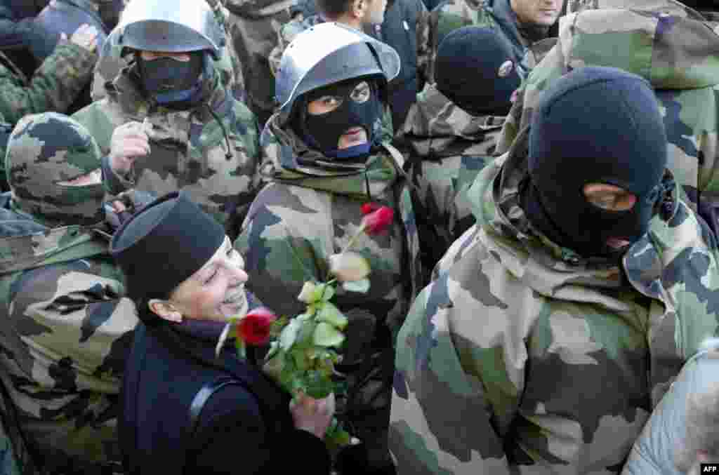 Грузинська жінка тримає квіти й посміхається у той час, як сили спецпризначення залишають позиції навколо президентської резиденції, не втручаючись у перебіг подій 