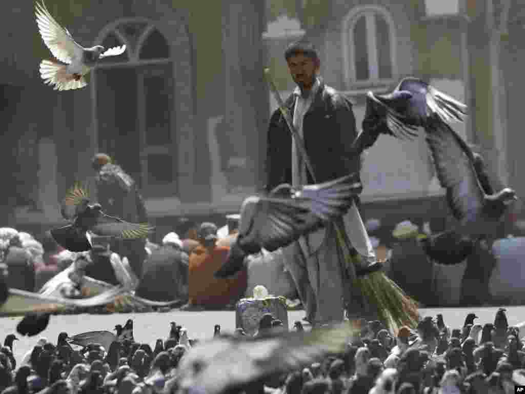 Afghan men sit outside a mosque preparing to pray as a road sweeper walks among flying pigeons during Friday Prayers in Kabul on June 17.Photo by Gemunu Amarasinghe for AP