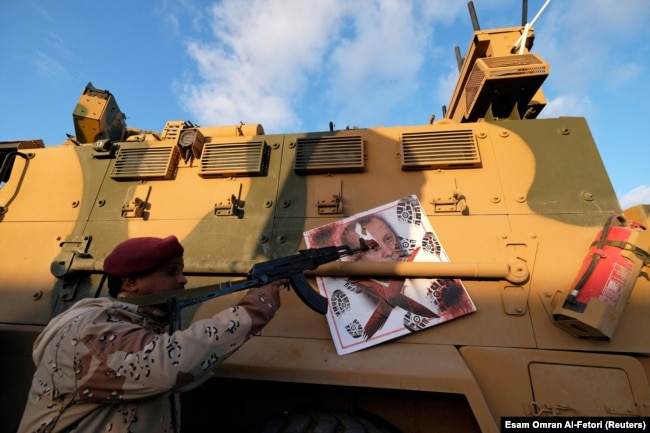 Боец Ливийской национальной армии Халифы Хафтара целится автоматом в портрет Реджепа Эрдогана на борту своего БТР. Город Сирт, июль 2020 года