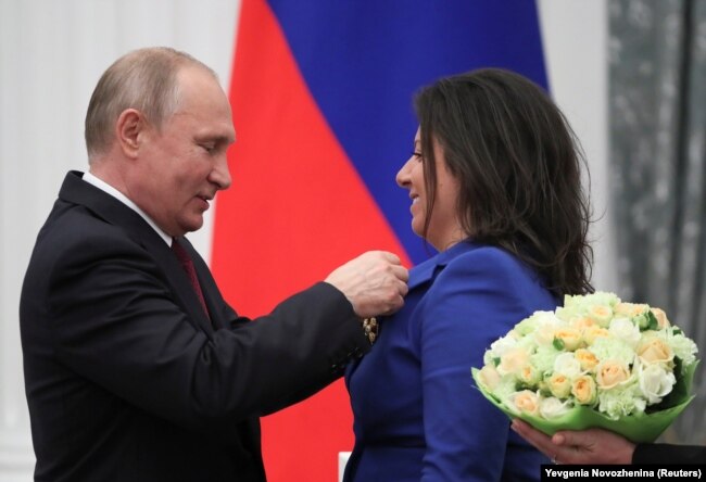 Президент Росії Володимир Путін нагороджує орденом Олександра Невського головного редактора телеканалу RT Маргариту Симонян. Москва, 23 травня 2019 року. У січні 2021 року Маргарита Симонян відвідала окупований Донецьк, де на форумі «Русский Донбас» закликала: «Россия, матушка, забери Донбасс домой!»