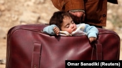 Një fëmijë duke fjetur në një valixhe, derisa largohet nga Guta Lindore