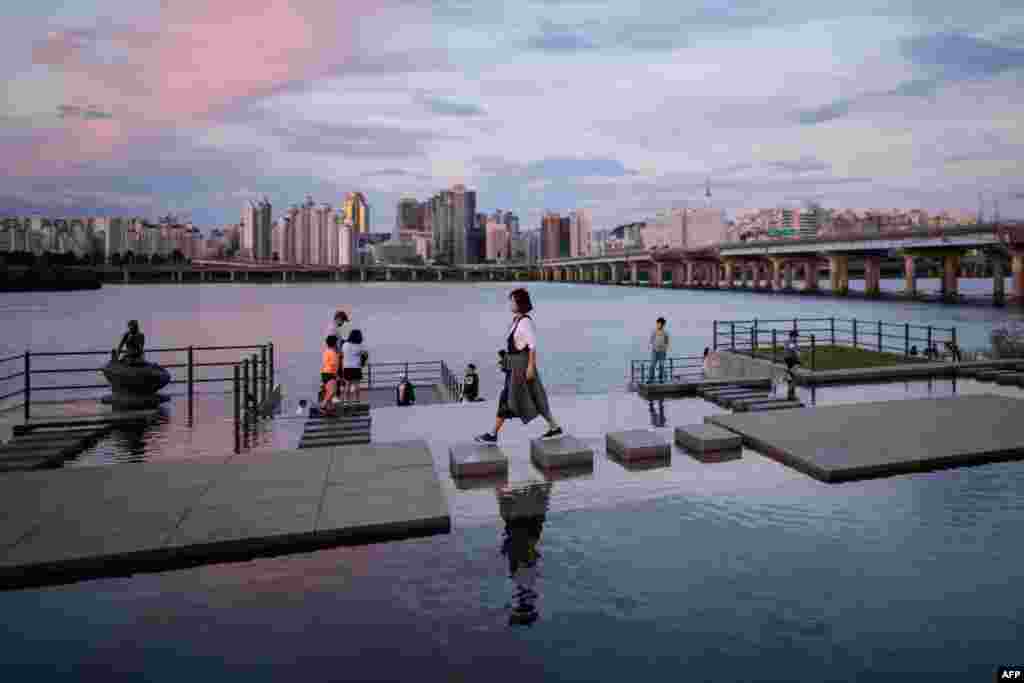 A Korean woman walks over stepping stones beside the Han River with Seoul&#39;s skyline in the background. (AFP/Ed Jones)