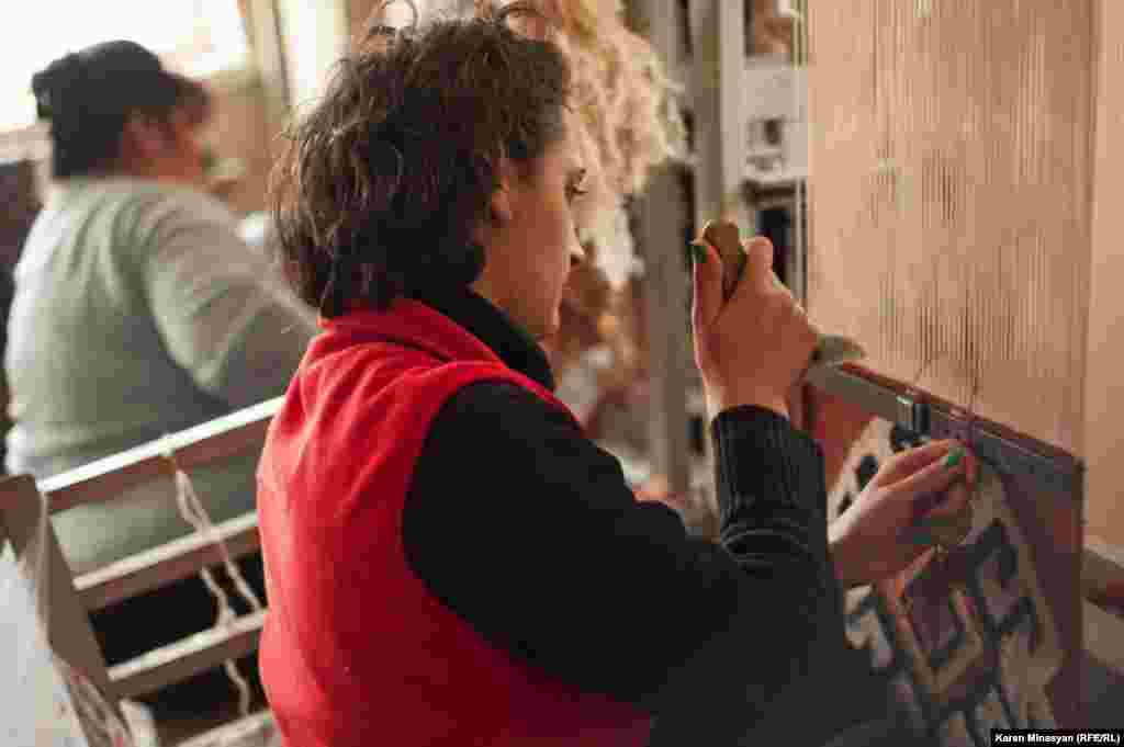 Women work on their carpet designs as they weave the rugs.