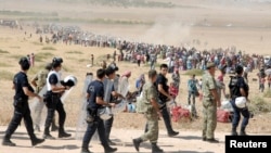 Turkish policemen and soldiers walk past Syrian Kurds waiting behind the border fence to cross into Turkey near the southeastern town of Suruc on September 19.