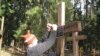 Ільля Копыль прымацоўвае шыльдачку на крыжы па сваім дзядзьку ў Курапацкім лесе 