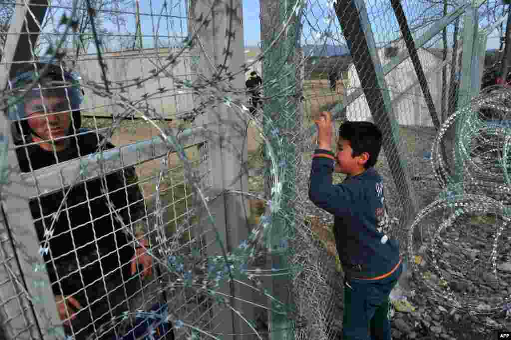 A Macedonian police officer looks on as young boy from Afghanistan cries and places his face against the fence at the Greece-Macedonia border during a demonstration near the village of Idomeni on February 22 after Macedonia closed the border to Afghan migrants. (AFP/Sakis Mitrolidis)