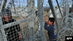 A Macedonian police officer looks on as young boy from Afghanistan cries and places his face against the fence at the Greece-Macedonia border during a demonstration near the village of Idomeni, February, 2016.