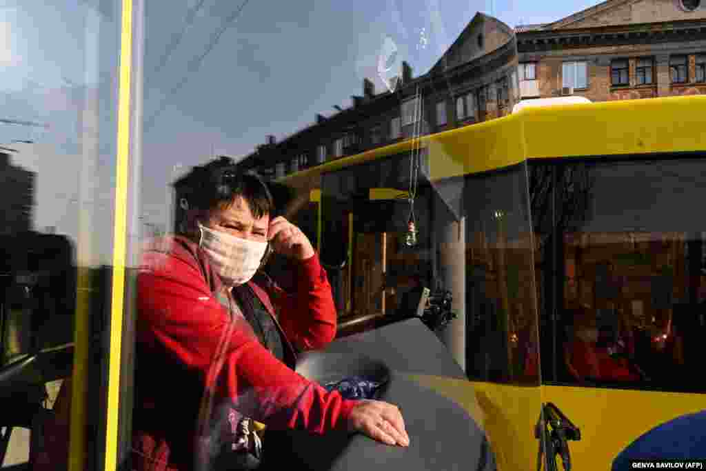 A conductor wearing a face mask looks out from a bus in Kyiv. Buses in the Ukrainian capital are limiting the number of passengers they can take on board. (AFP/​Genya Savilov) &nbsp;