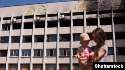 A mother and her baby walk in front of Mariupol's city hall in July 2015. The building had been badly damaged in fighting with Russia-backed separatists the previous year.