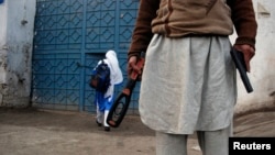 A man with a gun and a metal detector poses for photographers while he stands outside a school in Peshawar.