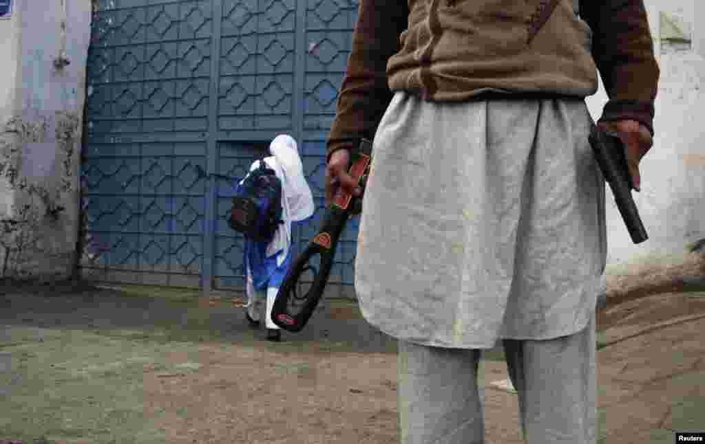A man with a gun and a metal detector poses for photographers while he stands outside a school after it reopened in Peshawar on January 12. (Reuters/Khuram Parvez)