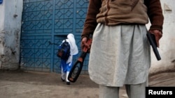 A man with a gun and a metal detector stands outside a school after it reopened in Peshawar on January 12.