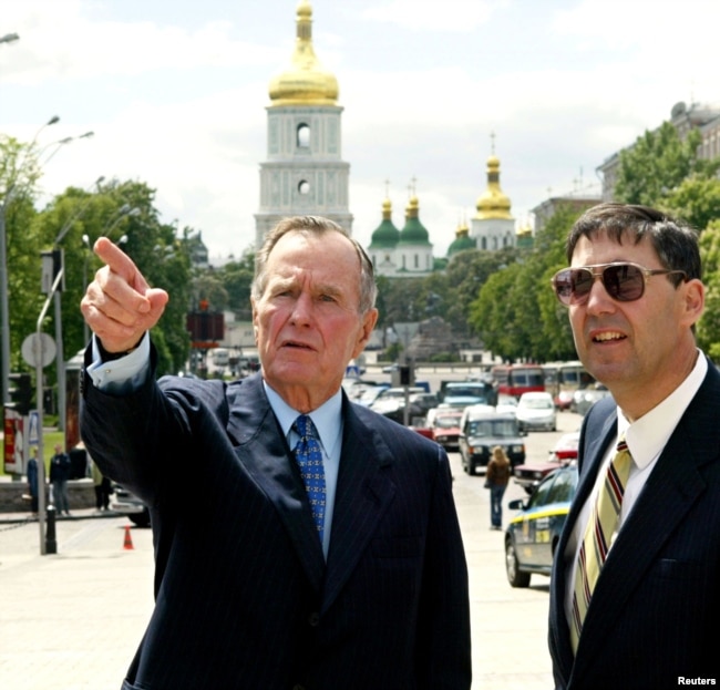 Колишній президент США Джордж Буш (ліворуч) під час приватної поїздки до України у центрі української столиці разом із тодішнім послом в Україні Джоном Гербстом. Київ, 21 травня 2004 року