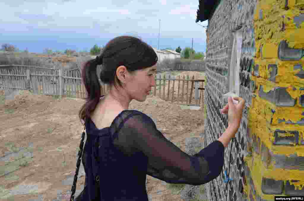 Местная жительница осматривает баню из стеклянных бутылок. Аул имени Турмагамбета Кармакшинского района.