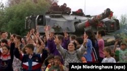 Shqiptarë etnikë festojnë para një tanku britanik të NATO-s, tytën e të cilit e kanë zbukuruar me lule, ndërsa trupat e para të NATO-s vendosen në kryeqytetin e Kosovës, Prishtinë, më 13 qershor 1999.