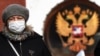 A woman wearing a protective face mask walks next to a Russian coat of arms at the Kalanchyovskaya railway station in Moscow on March 19. 