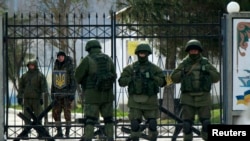 Ukraine -- Ukrainian servicemen ( back ) look from their military base as armed men, believed to be Russian servicemen, stand guard outside in the village of Perevalnoye near the Crimean city of Simferopol, March 10, 2014