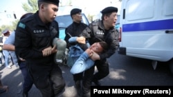 Полицейский спецназ несет задержанного к служебному микроавтобусу. Алматы, 21 сентября 2019 года.