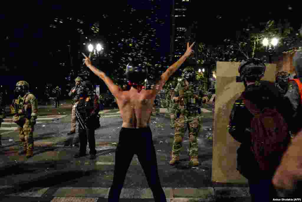 A topless protestor (C) gestures in front of federal police personnel in Portland, Oregon early July 26, 2020, as protests continue across the United States following the death in Minneapolis of unarmed African-American George Floyd. - Police and federal agents fired tear gas and forcefully dispersed protesters in the US city of Portland, amid President Donald Trump&#39;s heavily-criticized &quot;surge&quot; of security forces to major cities. The city, the biggest in the state of Oregon, has seen nightly protests against racism and police brutality for nearly two months, initially sparked by the death of unarmed African American George Floyd at the hands of police in Minnesota (Photo by Ankur Dholakia / AFP)