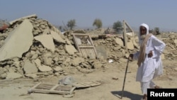 An earthquake survivor walks past the rubble of a mud-brick house in Awaran district.