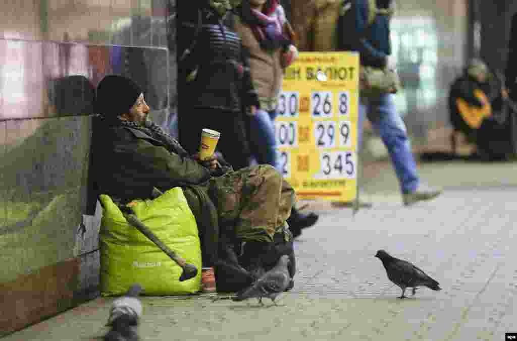 An elderly homeless Ukrainian man begs for money next to a sign showing exchange rates for the Ukrainian hryvnia against major international currencies inside an underground passage in downtown Kyiv. (epa/Sergey Dolzhenko)