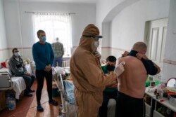 Лікар, одягнений у спеціальний костюм для захисту від коронавірусу, перевіряє пацієнта на коронавірус стетоскопом під час вечірнього огляду в лікарні в Почаєві, 1 травня 2020 року