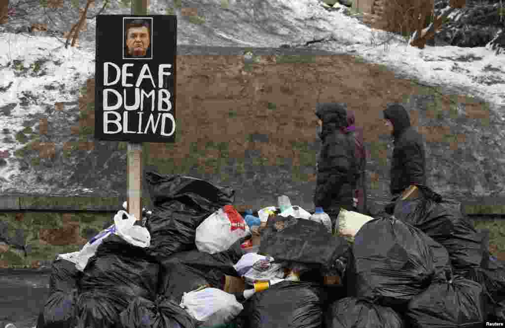 Ukrainians walk past a sign with a picture of President Viktor Yanukovych at a garbage-collection point at the site of clashes with riot police in Kyiv. (Reuters/Vasily Fedosenko)