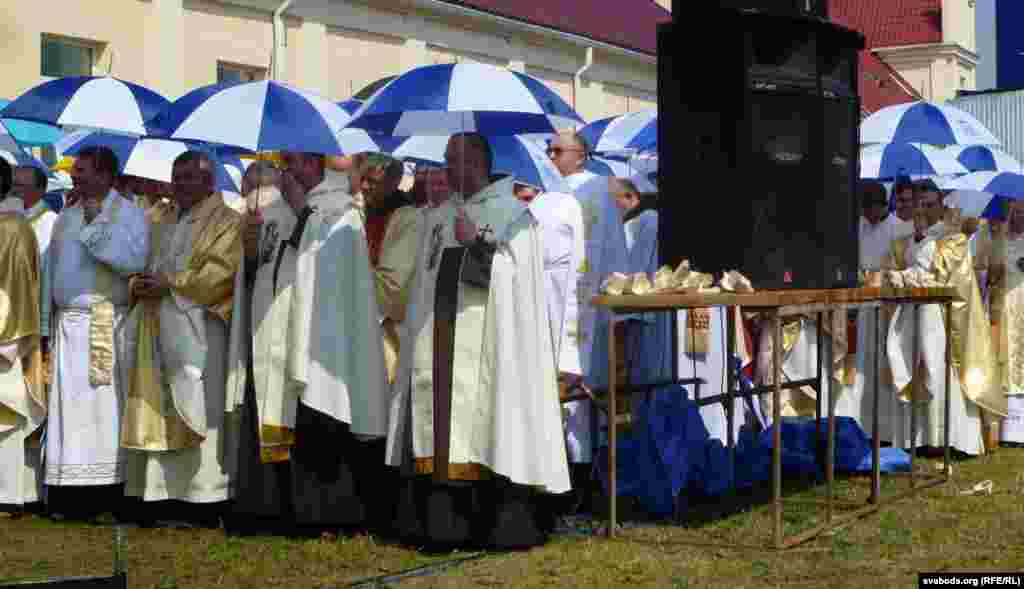 Clergy shelter under umbrellas during a pilgrimage in Budslau, Belarus, which houses the National Sanctuary of the Mother of God of Budslau.