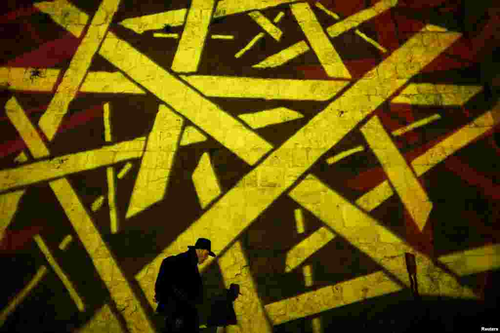 An Ultra-Orthodox Jewish man walks past an image projected onto a wall surrounding Jerusalem&#39;s Old City during the Hanukkah holiday on December 8.&nbsp;