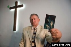 Священник Виталий Параскун показывает фотографию, снятую, когда он находился в плену. Он говорит, что не боялся умереть, когда его пугали стрельбой, и испугался, только когда угрожали раздробить колено, так как в камере была беременная крыса. Он не держит зла на своих мучителей. Он рад, что в плену ему удалось убедить четырех человек стать верующими