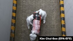 Медицинские работники в защитных костюмах несут в больницу больного коронавирусом. Сеул, 9 марта 2020 года.