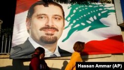 A woman and her daughter pass by a poster of Prime Minister Saad Hariri, in Beirut, Lebanon, Saturday, Nov. 11, 2017. 