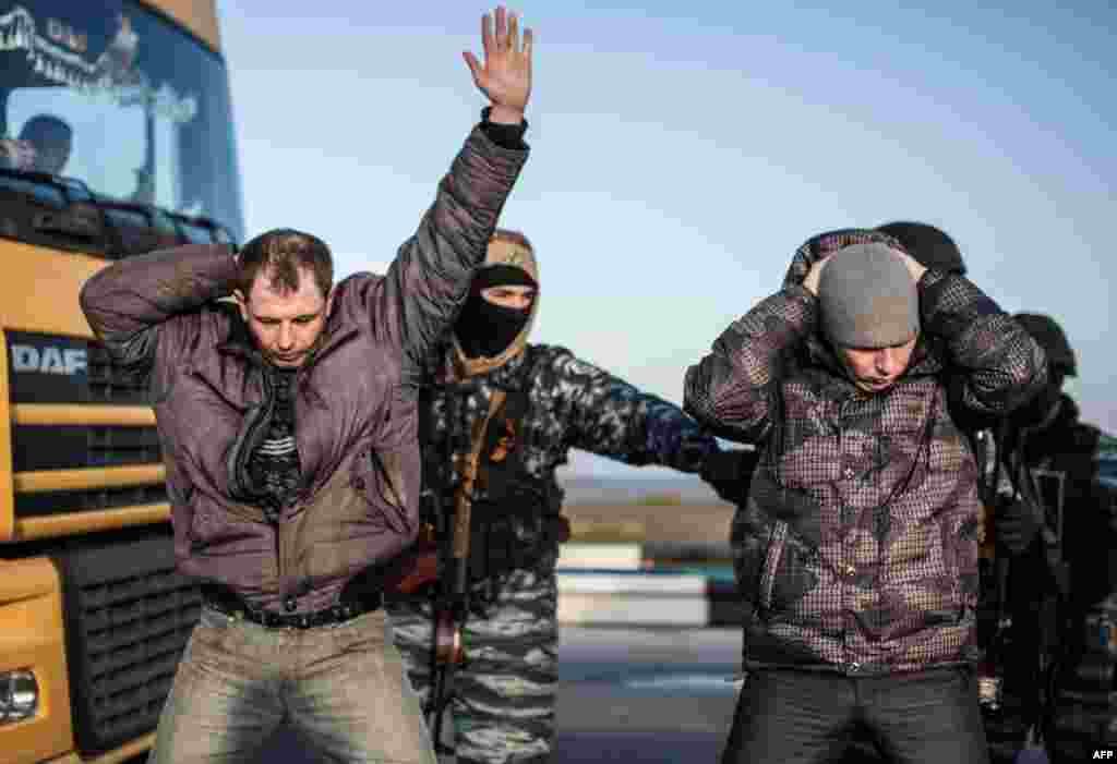 Men hold their hands on their heads as they are searched by pro-Russian servicemen at the Chongar checkpoint at the entrance to Ukraine's Crimea, which is currently occupied by Russian forces. (AFP/Alisa Borovikova)