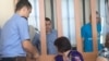 На судебном процессе трех жителей Шалкара, обвиняемых в «терроризме». Справа - Ергожа Амангожин, слева рядом с полицейским - Мейрамбек Турганбаев. Актобе, 11 августа 2016 года.