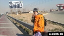 Mohammad Maleki, wearing a shawl that says "Let's Sweep Garbage," flashes the victory sign along a roadway outside the capital, where he and a colleague were dumped by security agents.