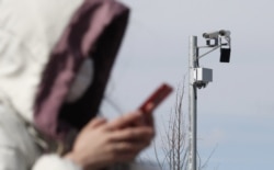 A woman wearing a face mask walks past a CCTV camera in Moscow.