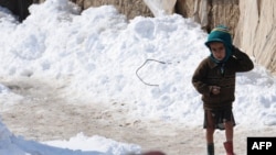 Мальчик в лагере бездомных в Афганистане идет по снегу. 