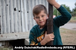 Davyd, 10, wants to be a lawyer and to go to sea. The fence behind their house in Luhanske is full of holes from a mine explosion.