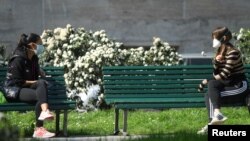Žene sa zaštitnim maskama na propisanoj udaljenosti sjede na klupama i razgovaraju, Milano, Italija, 21 mart 2020.