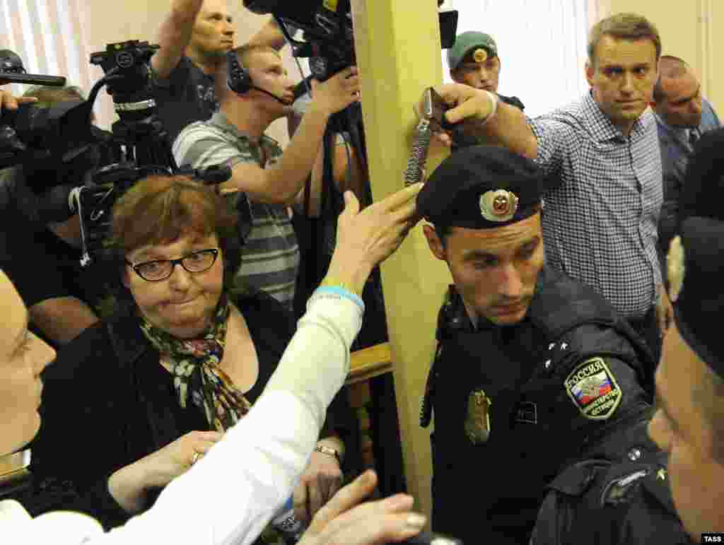 Aleksei Navalny passes his watch and phone to his wife as he is led away in handcuffs.