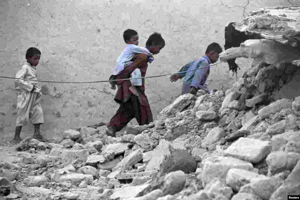 Earthquake survivors walk through the rubble of a mud house after it collapsed during the temblor in Awaran.