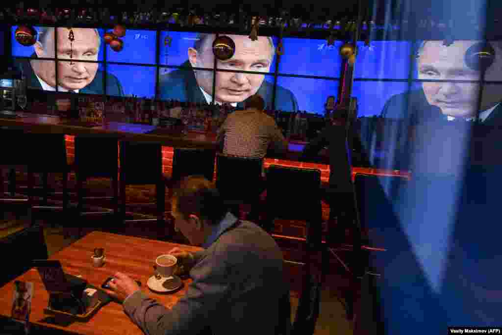 A man drinks coffee in front of screens broadcasting Russian President Vladimir Putin&#39;s annual press conference, at a bar in Moscow on December 20. (AFP/Vasily Maksimov)