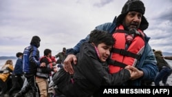 مردی پس از رسیدن قایق حامل ۵۴ پناهجوی افغان به ساحل جزیره لسبوس یونان به یک پسر کمک می‌کند تا راه برود. ۲۸ فبروری ۲۰۲۰ 