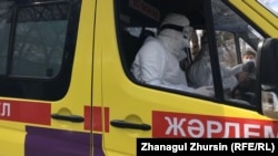 Медработник в защитной одежде и маске в автомобиле скорой помощи.