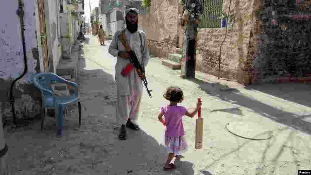 OCTOBER 24, 2012 -- A girl with a cricket bat walks past a bodyguard of the leader of the the highly secretive Sunni Muslim extremist group Lashkar-e Jhangvi holding a rifle on a street near Malik Ishaq's home in Rahim Yar Khan in Pakistan's southern Punjab Province. (Reuters/Mian Khursheed)