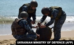 Украинские военные обезвреживают морскую мину, выброшенную на берег штормом, во время масштабного вторжения России в Украину. Это фото обнародовало Минобороны Украины 16 мая 2022 года